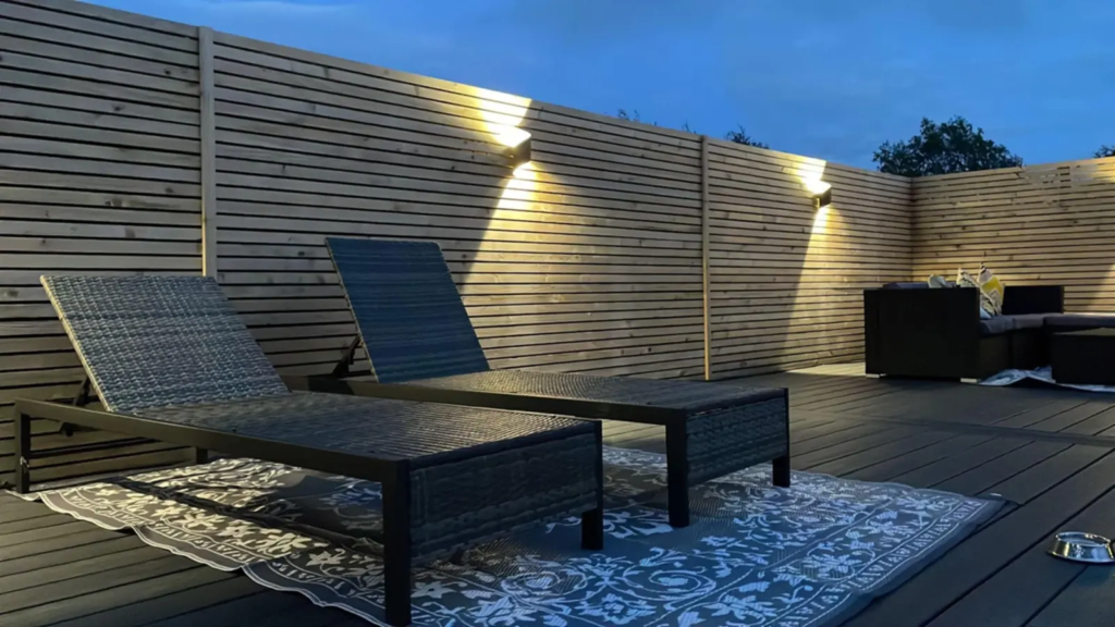 Dark Trex composite deck with sun loungers and wall lights at dusk