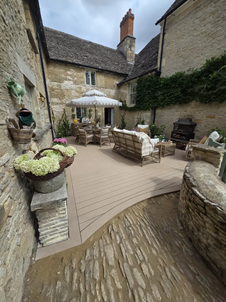Curved Trex deck sweeping around cobbles in a Cotswold stone courtyard