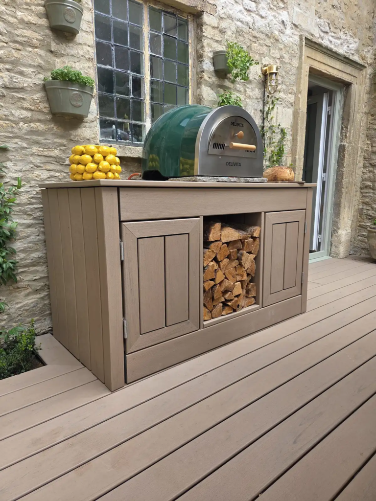 Bespoke Trex outdoor kitchen built around a pizza oven, with a log store