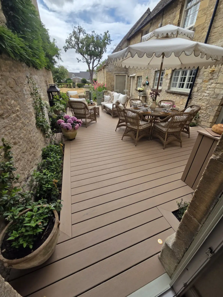 Symmetrical Trex deck with planters and a dining table in a Cotswold courtyard